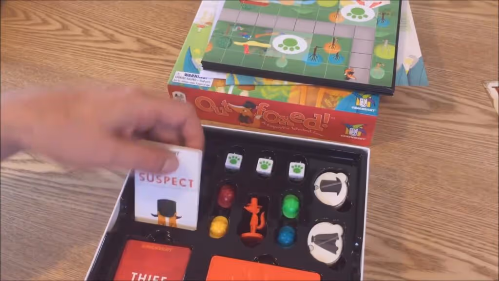 Outfoxed game box and components displayed showing the game board, decoder, suspects, and detective pieces
