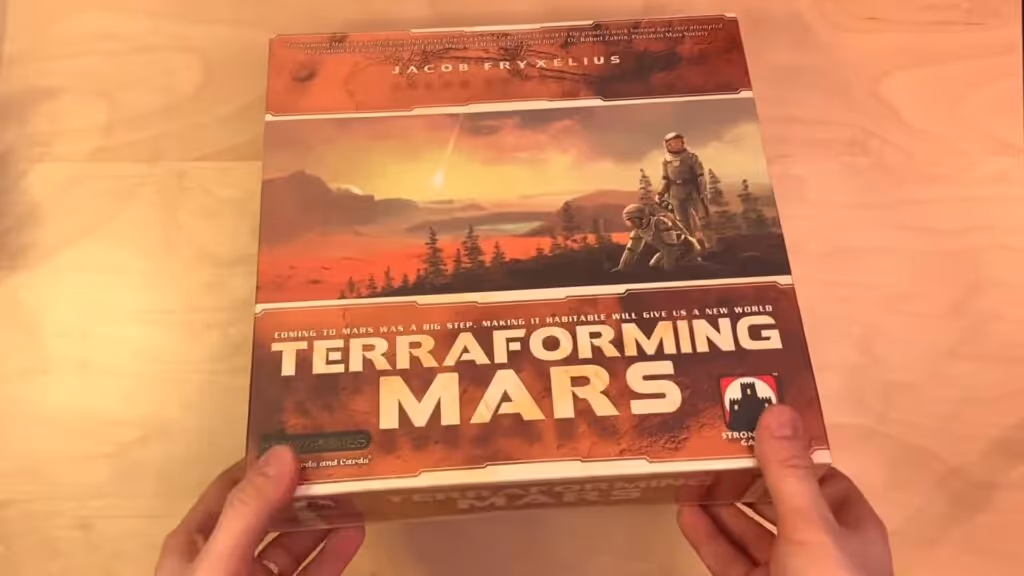 Box of the board game "Terraforming Mars" held by hands, featuring a Martian landscape with astronauts.
